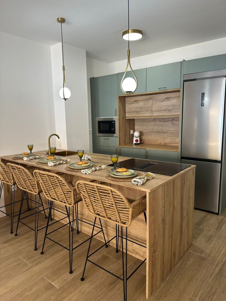 Cocina equipada con isla, muebles verde salvia y lámparas doradas